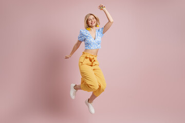 Full length of excited young woman jumping and smiling against pink background