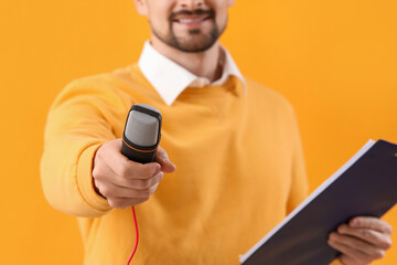 Male journalist with microphone and clipboard on yellow background, closeup