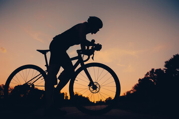 Fototapeta na wymiar Silhouette of a woman riding a bike during a sport cycling race on a sunset