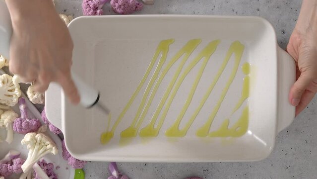 The chef poured olive oil on a white ceramic baking pan, flat lay. Oven-roasted cauliflower recipe.