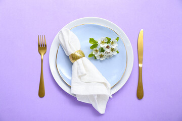 Beautiful table setting with folded napkin and blooming tree branch on lilac background