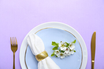 Beautiful table setting with folded napkin and blooming tree branch on lilac background