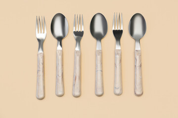 Stainless steel forks and spoons with plastic handles on beige background