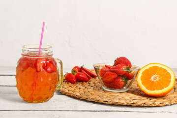 Mason jar of juice and bowl with strawberry on white wooden table