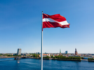 Huge Latvian flag flutters in the wind with Riga old town in the background in Latvia. Beautiful summer day. - obrazy, fototapety, plakaty