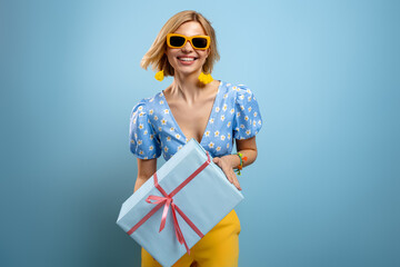 Beautiful young woman holding a gift box and smiling against blue background