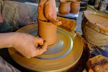 ceramics, workshop, ceramic art concept - close-up of man's hands forming a new vessel, man's fingers working with potter's wheel and raw edge, frontal close-up.