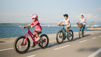 Fototapeta premium Mother with son and little daughter relaxed cycling on a coastal route, with a view out over the sea