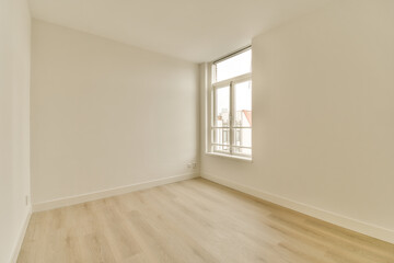 an empty room with white walls and wood flooring on the right, there is a window to the left
