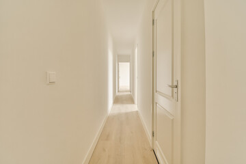 a long hallway with white walls and wood flooring on either side by side, leading to an open door