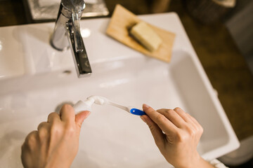 Female hand holding toothbrush with toothpaste applied on it in bathroom. Close up of female hand ready for brushing teeth. Young woman hand holding toothbrush with white tooth paste.