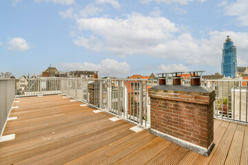 a rooftop with some buildings in the background and a blue sky filled with fluffy white clouds above it, as seen from an apartment