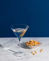 Classic martini and peanuts with a dark blue background and white marble counter
