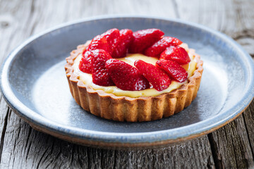 Strawberry tart, popular French pastry or Italian. Served on a plate placed on a rustic wooden table. Seasonal dessert. 