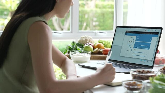 Woman Asian Professional Nutritionist working and checking data from a laptop with a variety of fruits, nuts, vegetables, and dietary supplements on the table