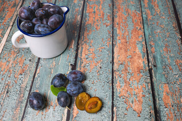 An enamel jug full of freshly harvested plums on old rustic wooden table top