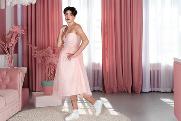 Portrait of a tender gay in a pink dress. Glamour homosexual young guy with makeup posing in a girly outfit.