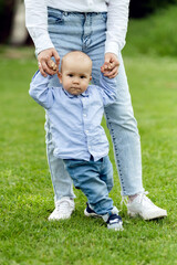 Fototapeta premium baby learns to walk holding mother's hands. walk with a little boy in nature. lovely one year old boy. child portrait
