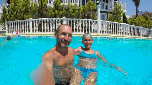 Active dad and child relaxation in home pool. A view of active smiling father with her daughter relax in the turquoise swimming pool in summer.