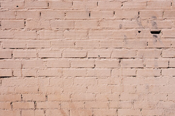 An old wall of different bricks painted in light red with some holes. Cement and bricks background texture