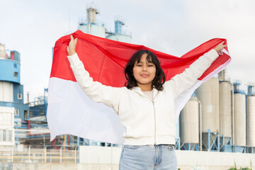 Smiling teenage girl with the flag of Indonesia on the background of a modern factory