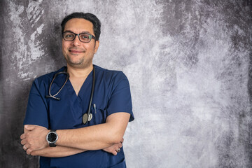 Portrait of a young smiling doctor in glasses with a stethoscope against a gray wall. Space for text.