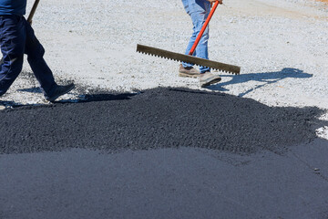 Fototapeta na wymiar Workmen working on pavement of road are laying asphalt while shoveling black gravel, preparing it for the paving