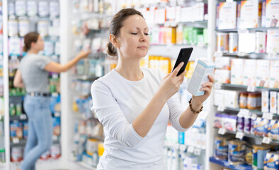 In pharmacy female visitor scan QR Code and reads composition of cream for problematic teenage...