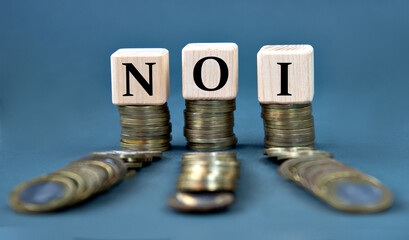 NOI - acronym on wooden cubes against the background of stacks of coins