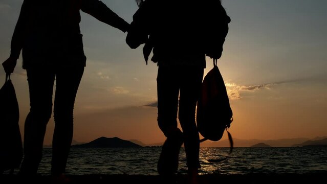 Silhouette of tourists females. Child with mom with backpacks at sunset.