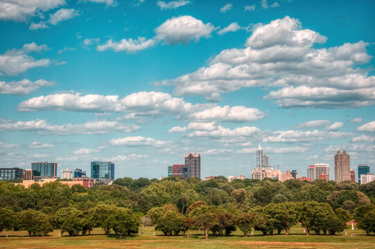A wide-angle Raleigh, North Carolina skyline with puffy clouds in a light blue sky.