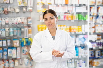 In pharmacy, positive female chemist stands and waits for visitors. Wide range of prescription and...