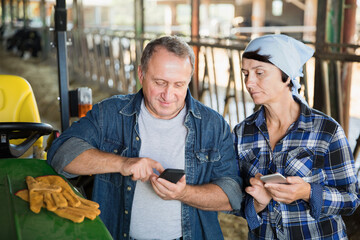 Senior spouses man and female farmers using phones on farm
