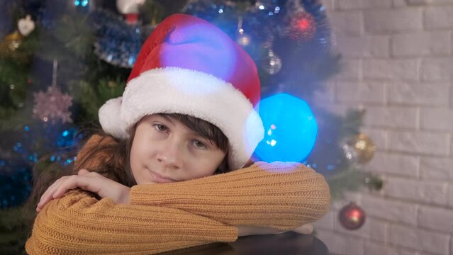 Warm teen Christmas in loneliness. A happy teen girl in red hat wait for party in festive Christmas room.
