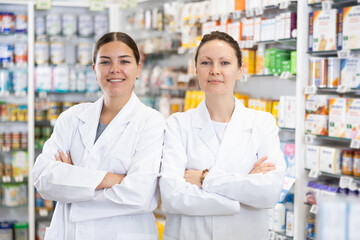 Portrait of two friendly positive pharmacists in interior of a pharmacy or a store selling healing cosmetics