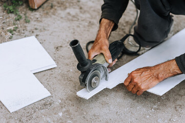 A man, a worker in an outdoor workshop, cuts off a plastic white material for insulation with a grinder, an electric cutter. Photography, industry.