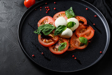 Caprese salad Italian cuisine concept  Tomato and mozzarella slices with basil leaves  on black ceramic platwantipasta black textured background close up