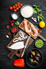 Uncooked spanish paella ingredients with king prawns, cuttlefish, mussels and herbs over black...