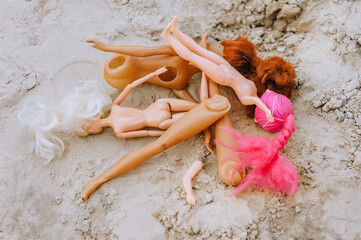 Broken dolls, discarded unnecessary plastic parts of toys lie in the sand on the playground in the...