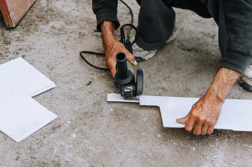 A man, a worker, cuts off plastic material for insulation with a grinder, an electric cutter.