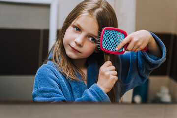 Red-haired teen girl, child combing her hair, taking care of herself, looking in the mirror in the...