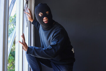 The robber in a black mask at the window of the apartment.