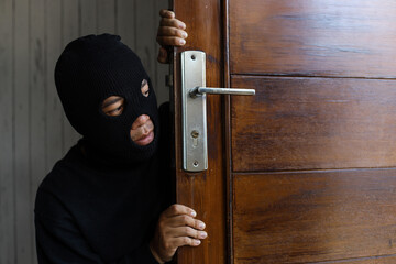 Thief robber spying and hiding behind a wooden door. Criminal activity