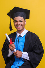 Young Asian man wearing graduation cap and ceremony robe holding diploma certificate with happy face smiling