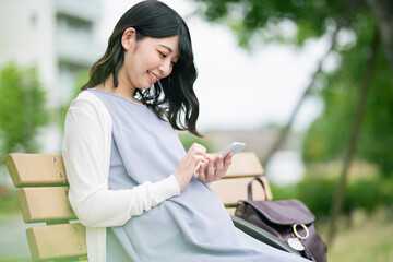 公園でスマートフォンを見る妊婦