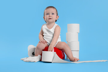 Little child sitting on baby potty and stack of toilet paper rolls against light blue background