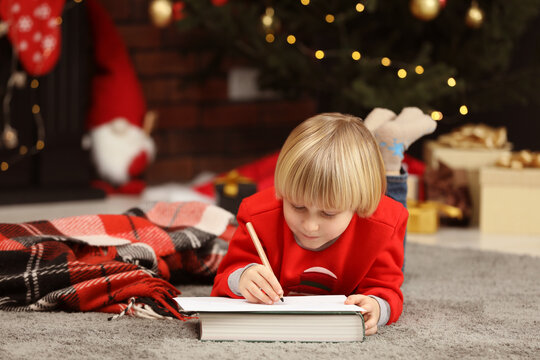 Little child writing letter to Santa Claus on floor at home. Christmas celebration