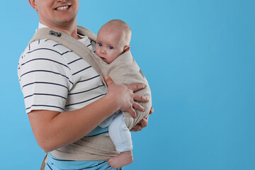 Father holding his child in sling (baby carrier) on light blue background, closeup. Space for text