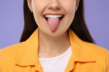 Obraz na płótnie Canvas Happy young woman showing her tongue on purple background, closeup
