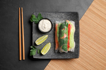 Delicious rolls wrapped in rice paper served on black table, flat lay